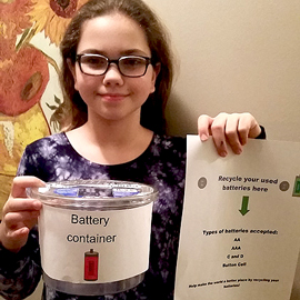 An OSBRC student holds up her battery recycling container and poster she made to complete mission 1