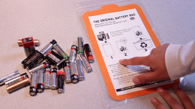A person is pointing to the instructions on a battery recycling bag that explain how to participate in three steps. Step 1, round up your used household batteries. Step 2, place your household batteries inside the plastic bag securing it with the zip tab. Make sure you tape the positive terminals on rechargeable batteries, as well as any lithium batteires. Step 3, place the recycle bag containing the batteries at the curb with your regular recycling during a week advertised by the municipality.