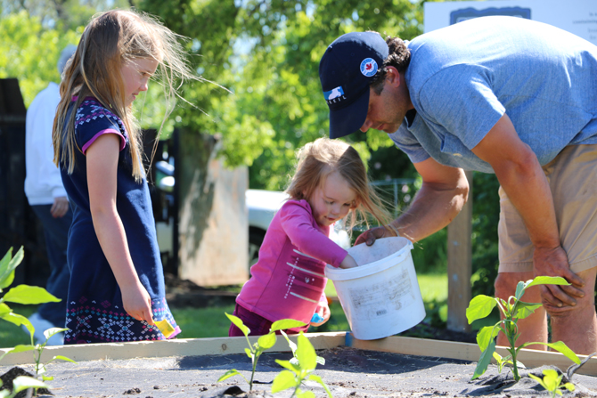 Jordan Elliott of Marine Recycling Corporation helps a youngster plant seedlings at the Lockview Park Community Garden in Port Colborne in support of the Port Cares Food Bank.