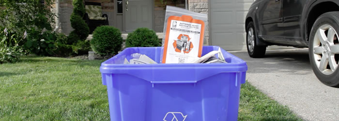 Picture of a zip lock bag being setout with a recycling box during a special curbside battery collection. This program is only offered by some municipalities during certain times of year. Batteries should never be place insdide blue boxes loose, or setout with recycling outside of these special events.